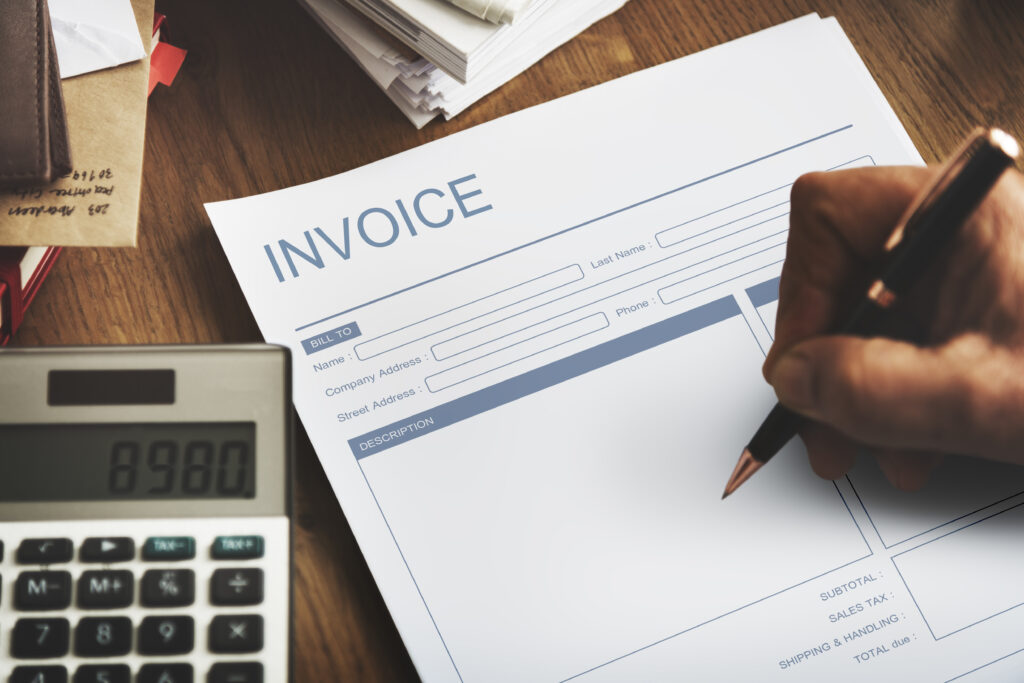 Factura en blanco con secciones para completar datos fiscales, acompañada de una calculadora y documentos administrativos. Representa el proceso de facturación y cálculo de la base imponible.